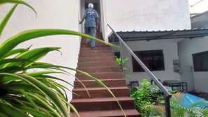 A person ascending a staircase with metal railings, surrounded by greenery and a white building with a window and a door. - Kalan Villa (Galle)