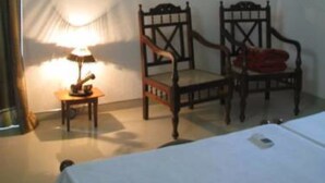 A room with a bed, two wooden chairs, a small table with a lamp, an air conditioning unit, and a window with curtains. - Kalan Villa (Galle)
