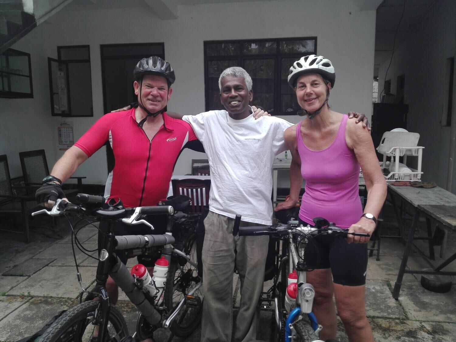 Three people standing next to bicycles in an outdoor setting with a building in the background.