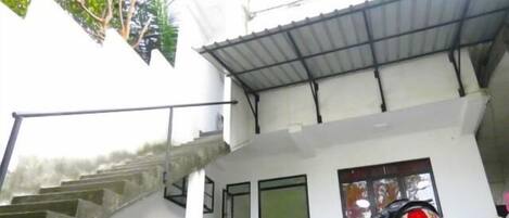 A two-story building with a staircase leading to the upper floor. There is a covered area with a metal roof, and a motorcycle parked outside.