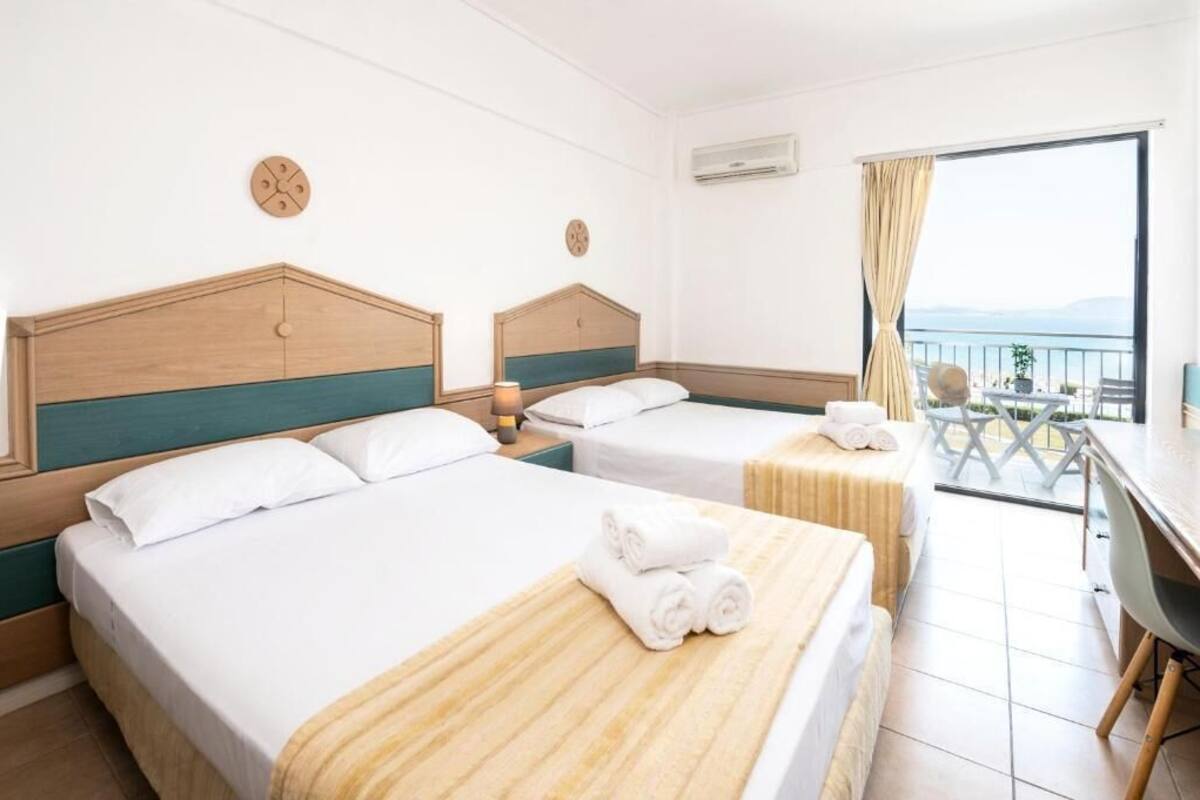 Habitación de hotel con dos camas, un escritorio y un balcón con vistas.