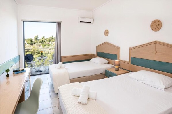 Habitación de hotel con dos camas, un escritorio, una silla y un balcón con vistas.