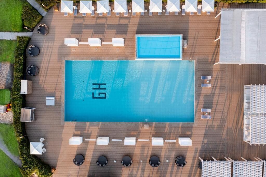An aerial view of a hotel pool area with a large pool, sun loungers, and a smaller pool.