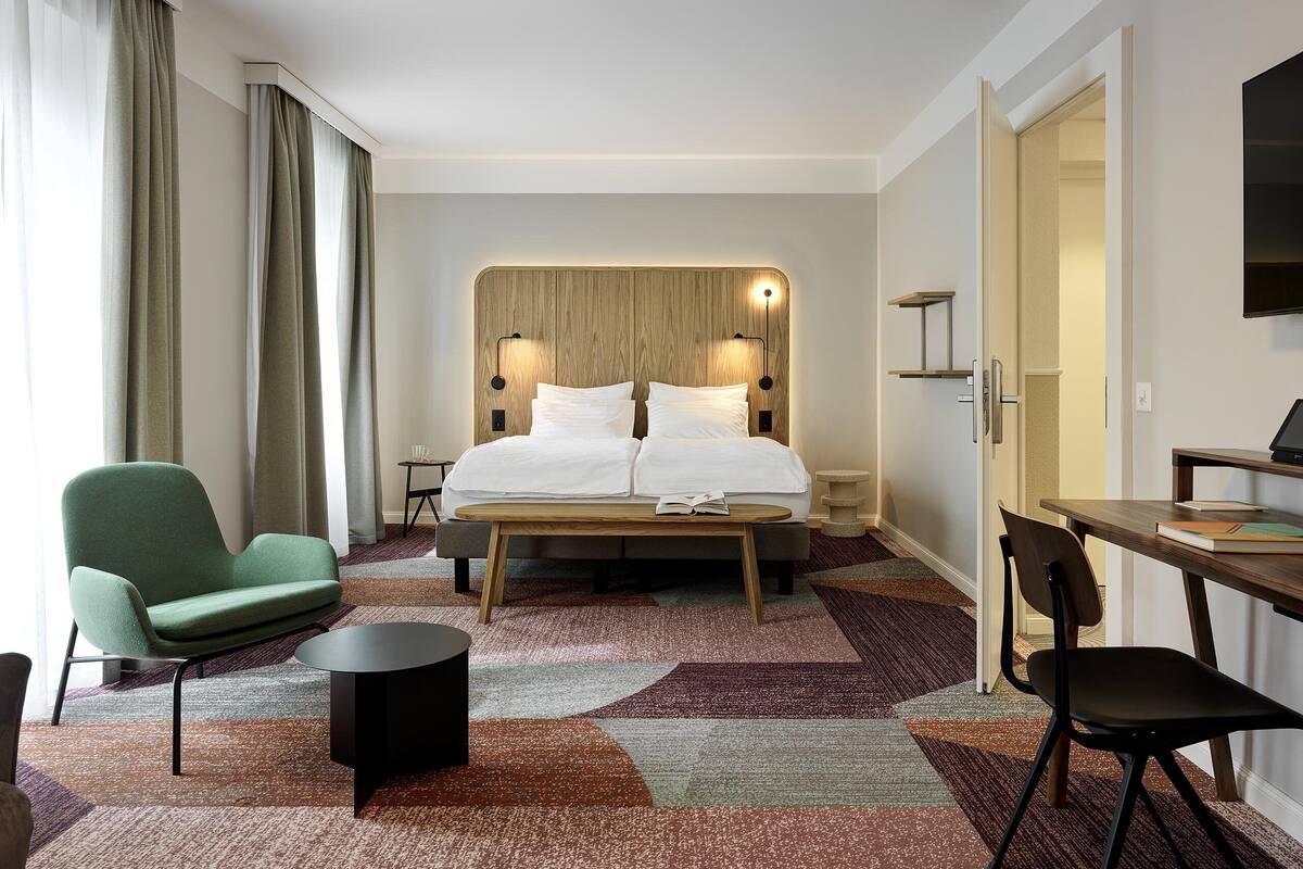 A hotel room with a bed, a desk, a chair, a small table, and a TV.