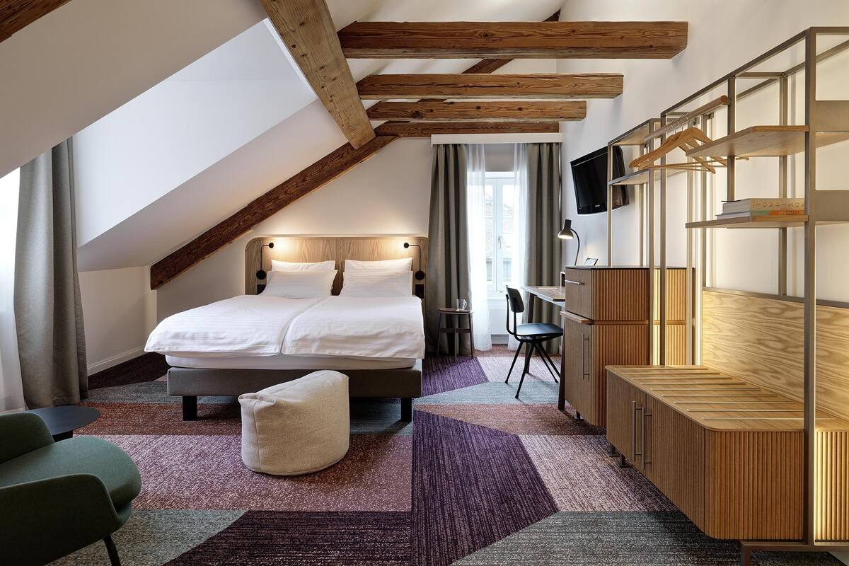 A bedroom with a loft-style ceiling, a bed, a desk, a TV, and a bookshelf.