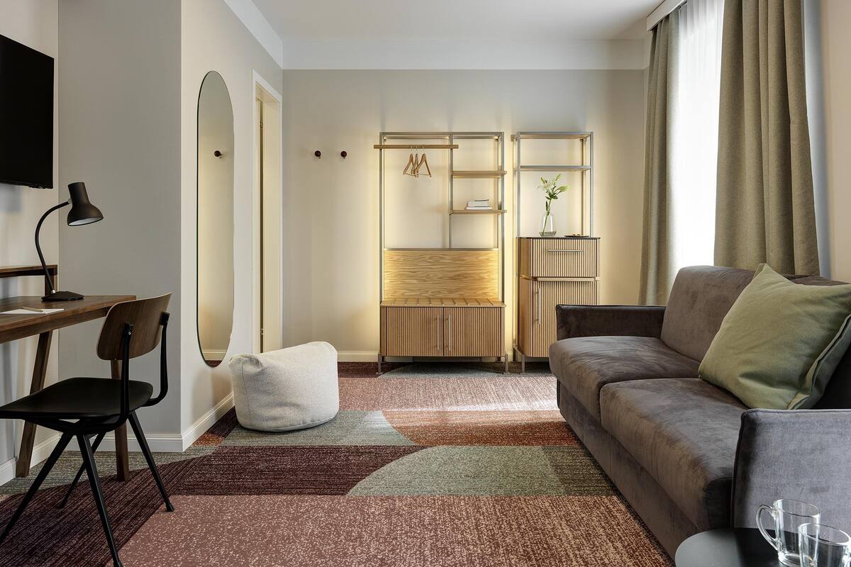 A modern living room with a sofa, a desk with a chair, a TV, and a bookshelf.