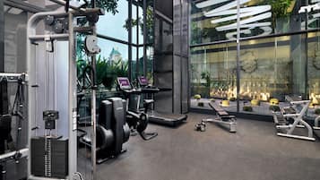 A modern gym with various exercise equipment, large windows, and a view of a building with a green roof.