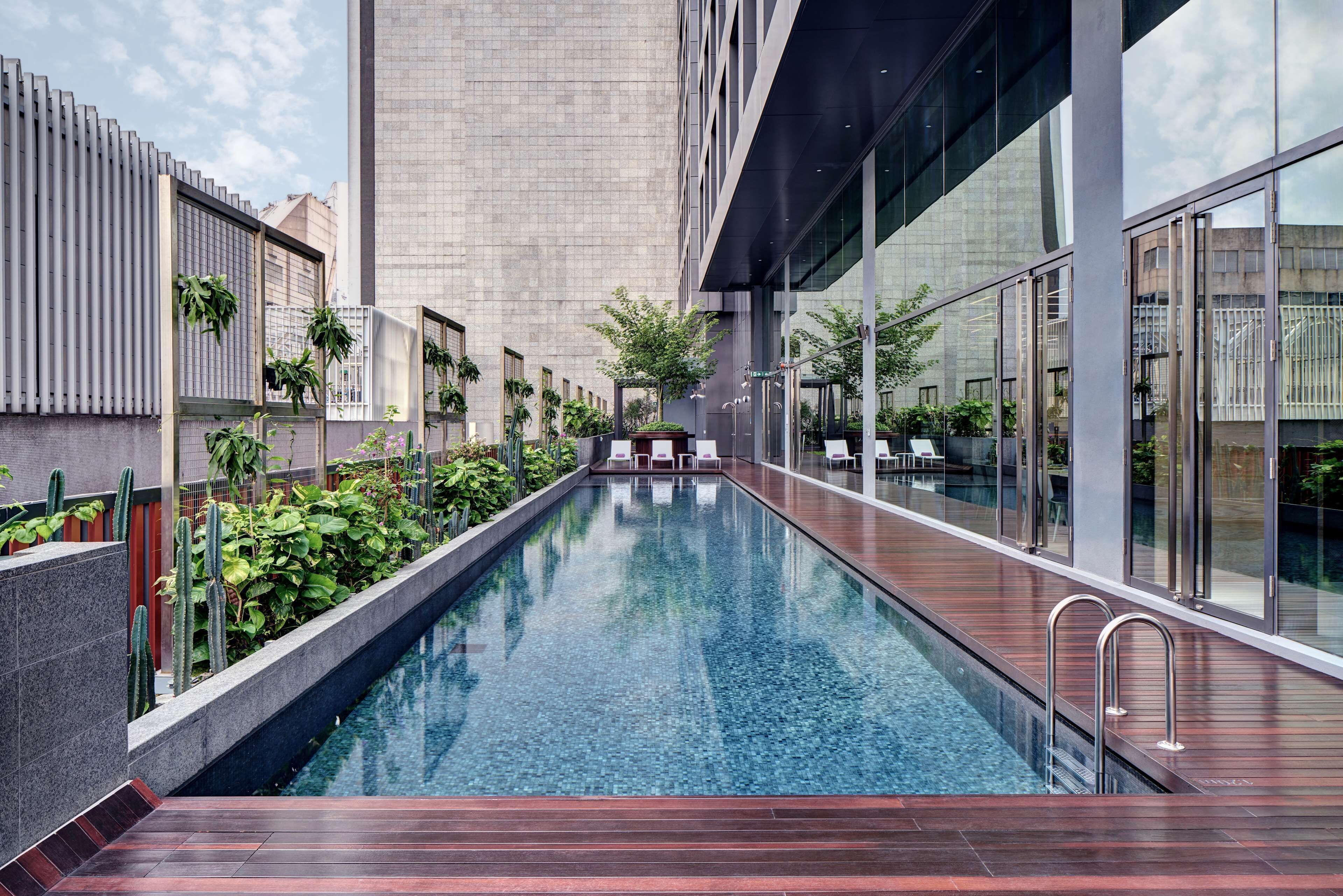 Una piscina interior moderna amb un pont de fusta, envoltada de vegetació i una paret de vidre.