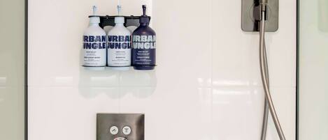 A modern bathroom with a glass shower enclosure, a handheld showerhead, and three bottles of Urban Jungle products.