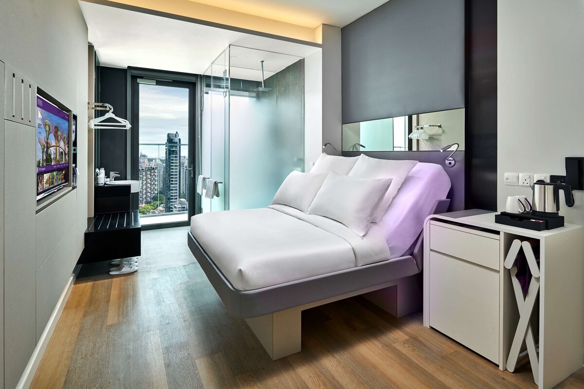 A modern bedroom with a bed, a desk, and a view of the city.