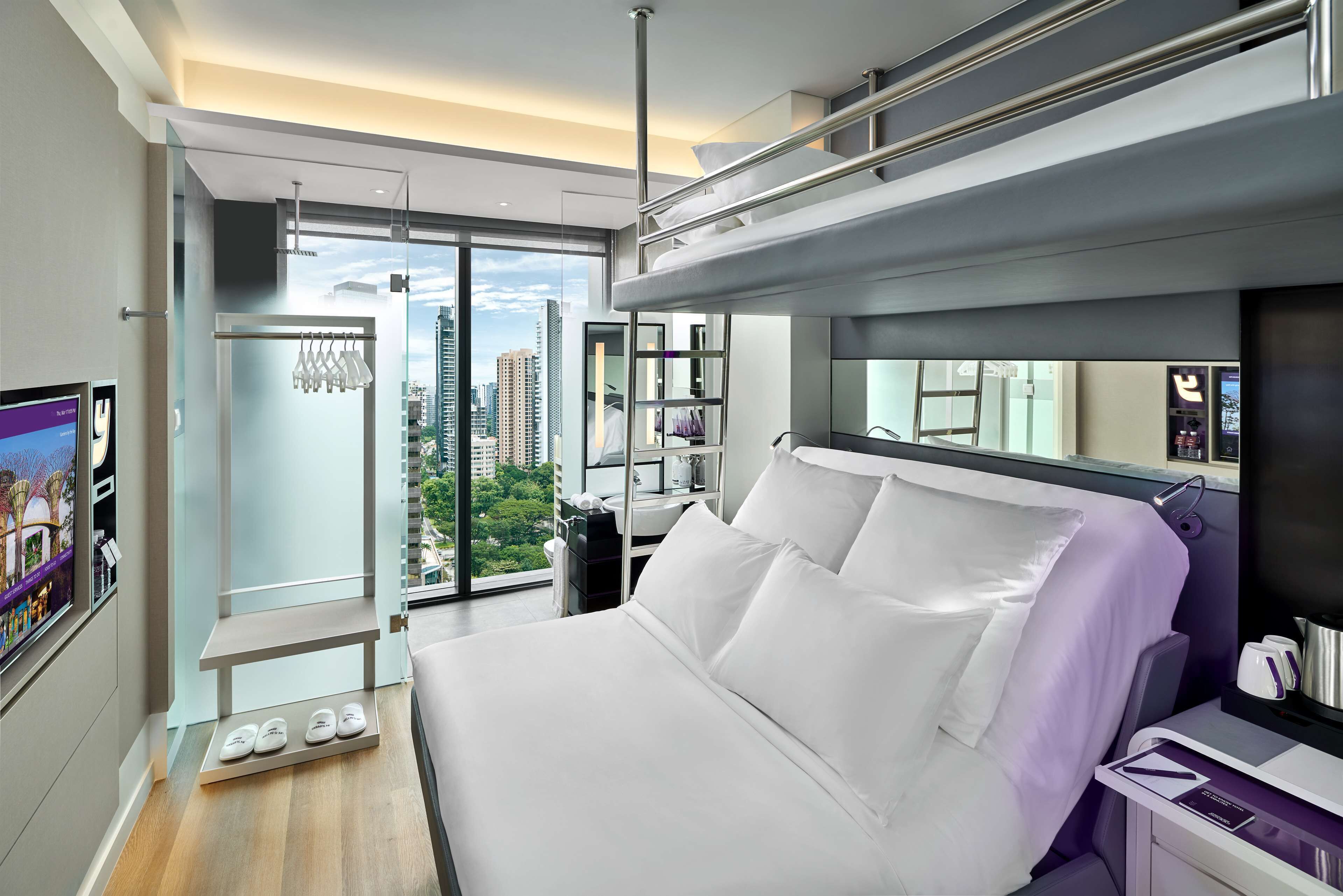 A modern hotel room with a large bed, a bathroom with a mirror, and a view of the cityscape.