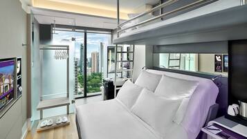 A modern hotel room with a large bed, a bathroom with a mirror, and a view of the cityscape.