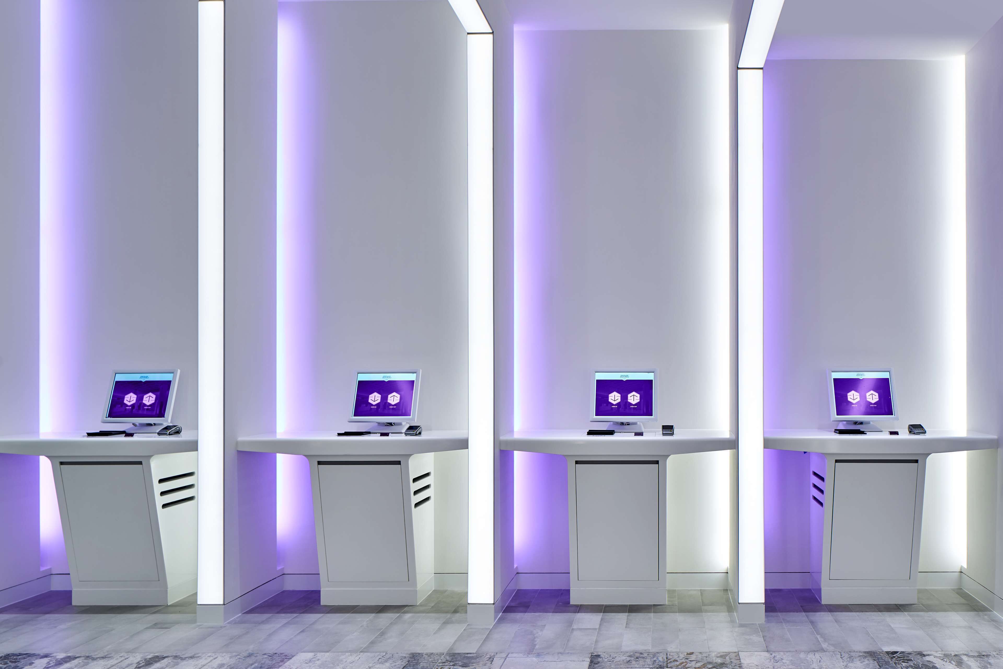 A modern, minimalist room with four desks, each with a computer monitor displaying a purple interface.