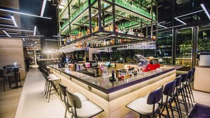 A modern bar area with a central island, bar stools, and shelves stocked with bottles and glasses. - YOTEL Singapore Orchard Road (Singapore)