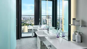 A modern bathroom with two sinks, a large mirror, and a view of a cityscape through floor-to-ceiling windows.