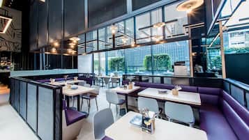 A modern restaurant interior with high ceilings, large windows, and a mix of seating arrangements including booths and tables.