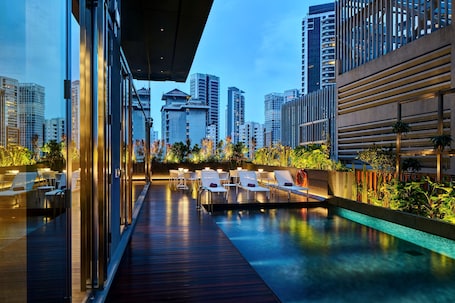 A rooftop pool area with lounge chairs and a view of surrounding high-rise buildings.