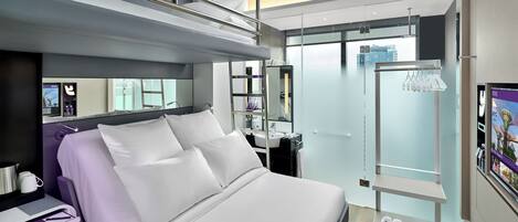 A modern hotel room with a bed, bedside table, and a view of the cityscape.