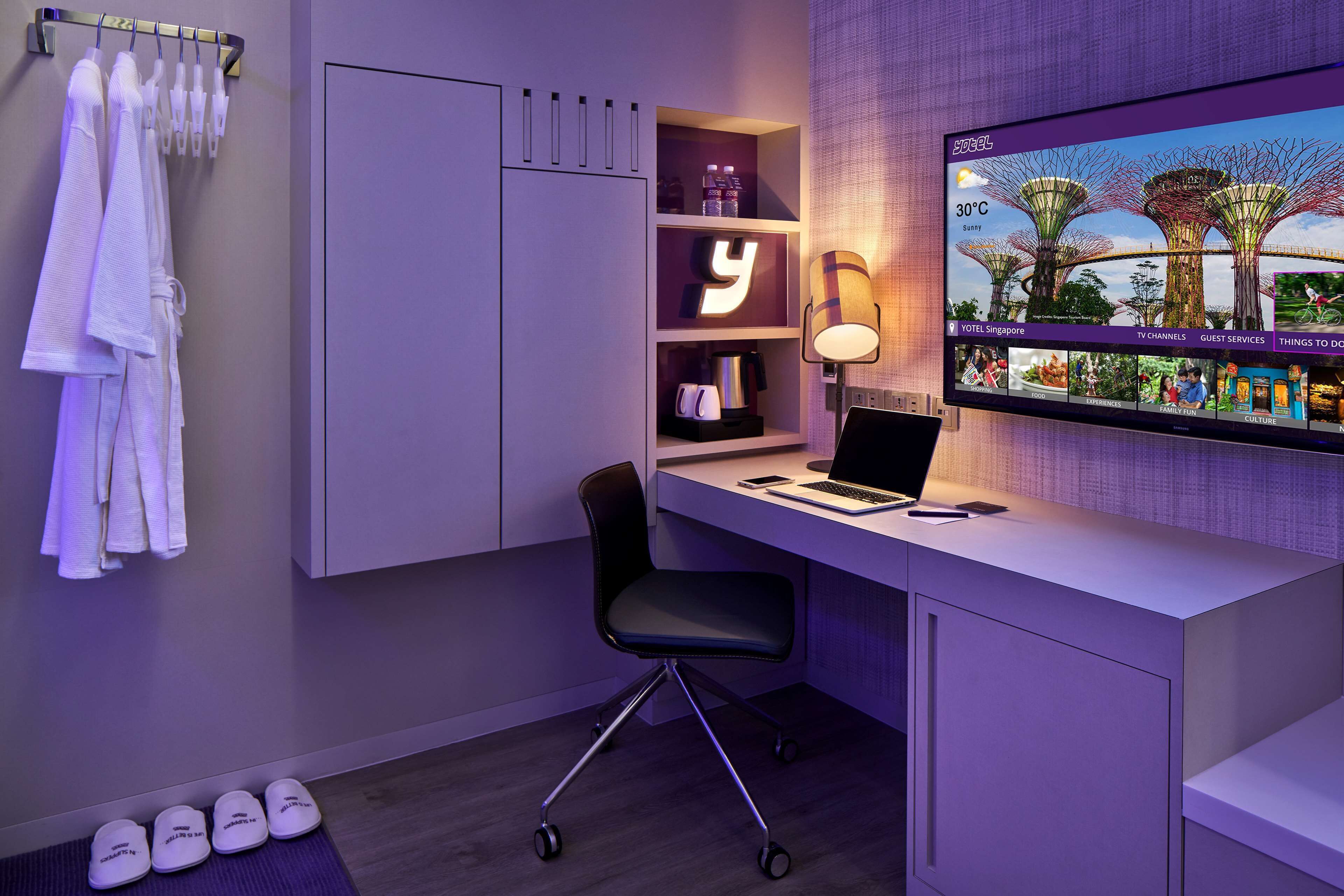 Una camera d'albergo moderna con una scrivania, un portatile e una TV che mostra un paesaggio tropicale.