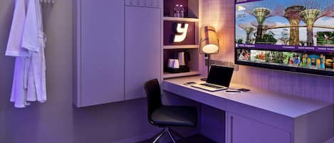 Una habitación de hotel moderna con un escritorio, una computadora portátil y un televisor que muestra un paisaje tropical.