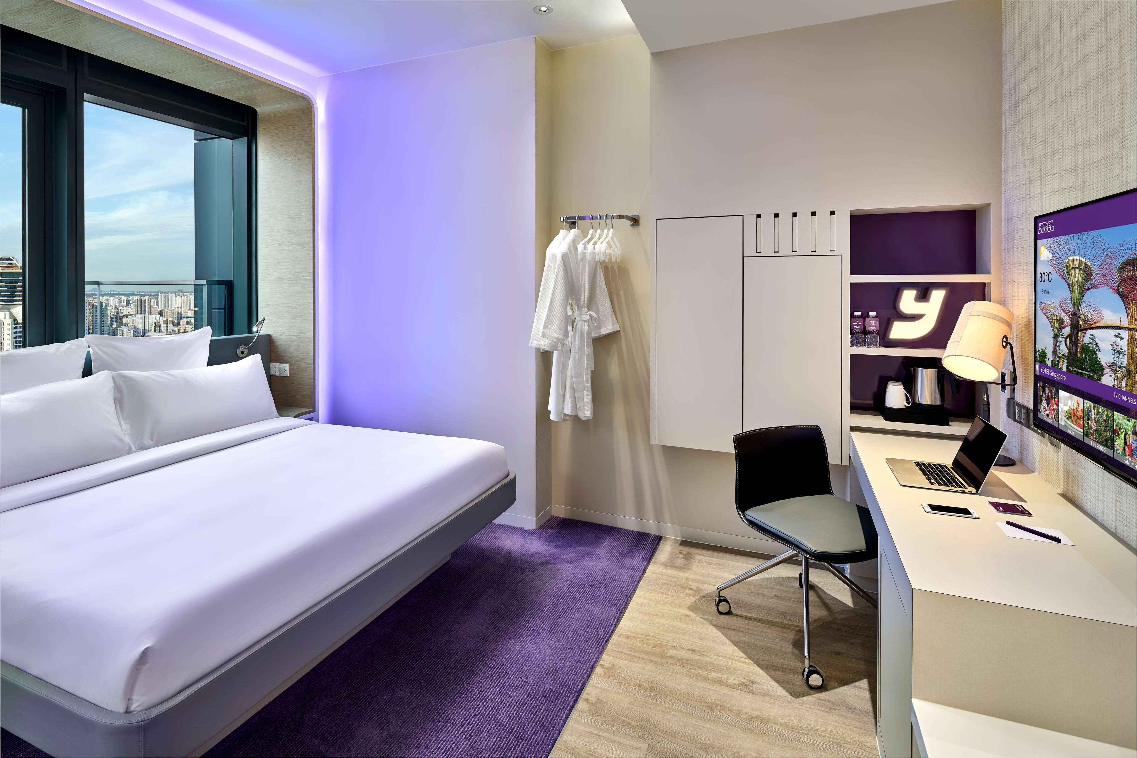 Une chambre d’hôtel équipée d’un lit, d’un bureau, d’une chaise et d’un téléviseur affichant les prévisions météorologiques.