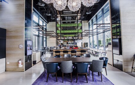 A modern dining area with a long wooden table, multiple chairs, and a bar in the background.