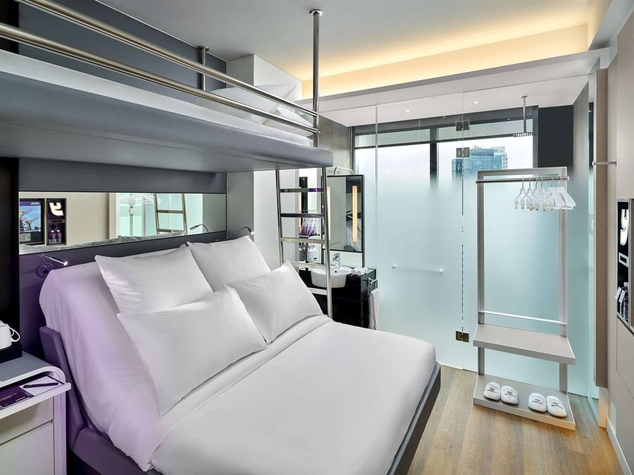 Moderni hotellihuone, jossa on sänky, peilipöytä, suihku ja näkymä kaupunkiin.