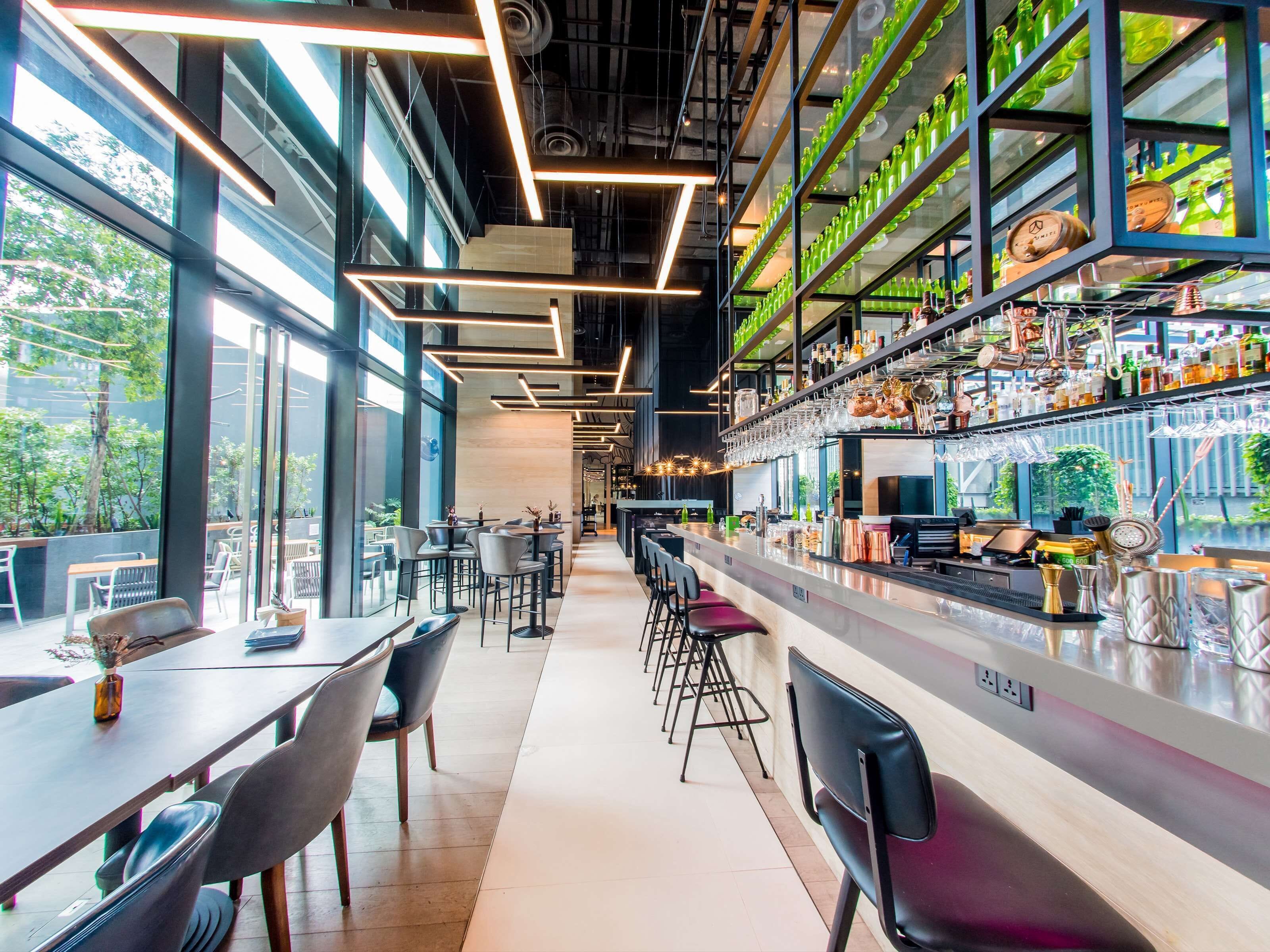A modern bar area with a long counter, bar stools, and shelves stocked with bottles and glasses.