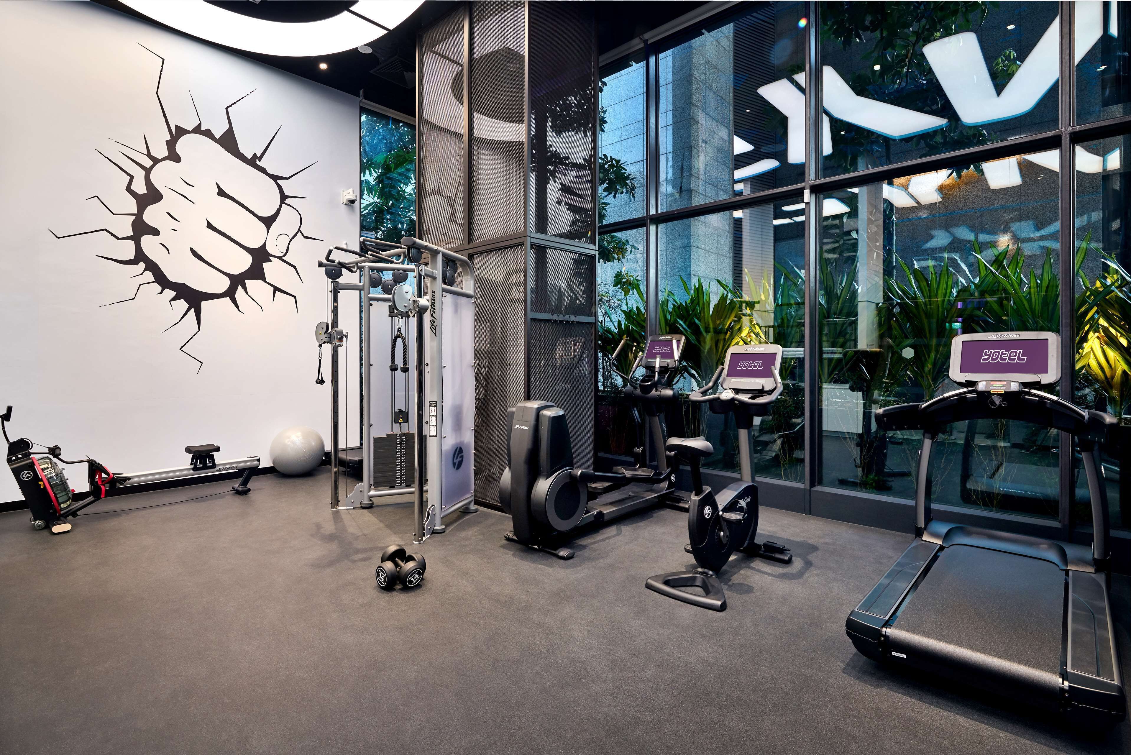 Ett modernt gym med olika typer av träningsutrustning, inklusive en roddmaskin, en crosstrainer och löpband.
