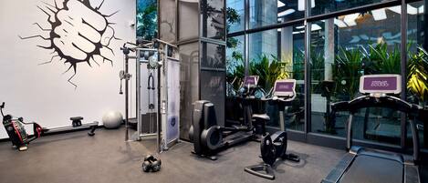 Ett modernt gym med olika typer av träningsutrustning, inklusive en roddmaskin, en crosstrainer och löpband.