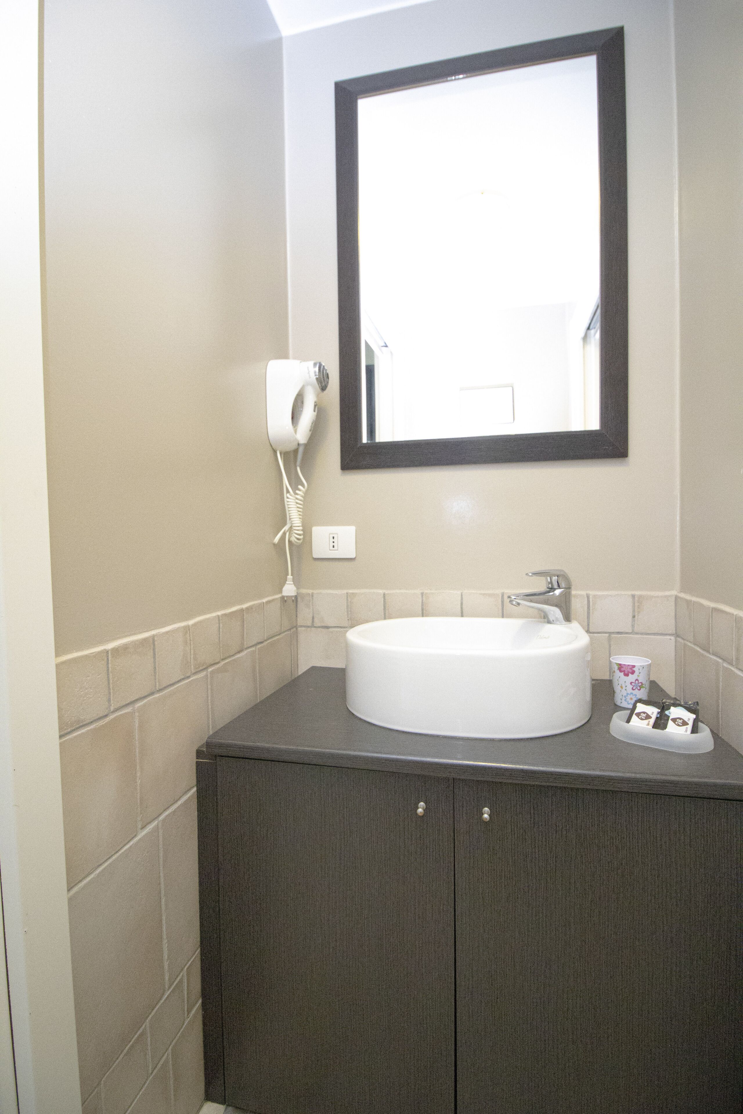 A bathroom with a white sink, dark cabinets, a mirror, and a hairdryer on the wall.