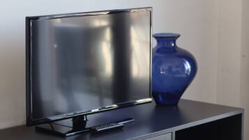 Un meuble noir pour téléviseur, sur lequel est posé un téléviseur à écran plat, et un vase bleu.