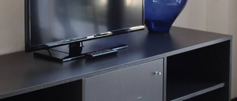 A black TV stand with a flat-screen TV and a blue vase.