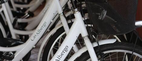 A row of white bicycles with "CasAlbergo" branding, each equipped with a black basket, parked indoors.