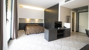 Una habitación de hotel moderna con cama, escritorio con televisor, una silla y una puerta.