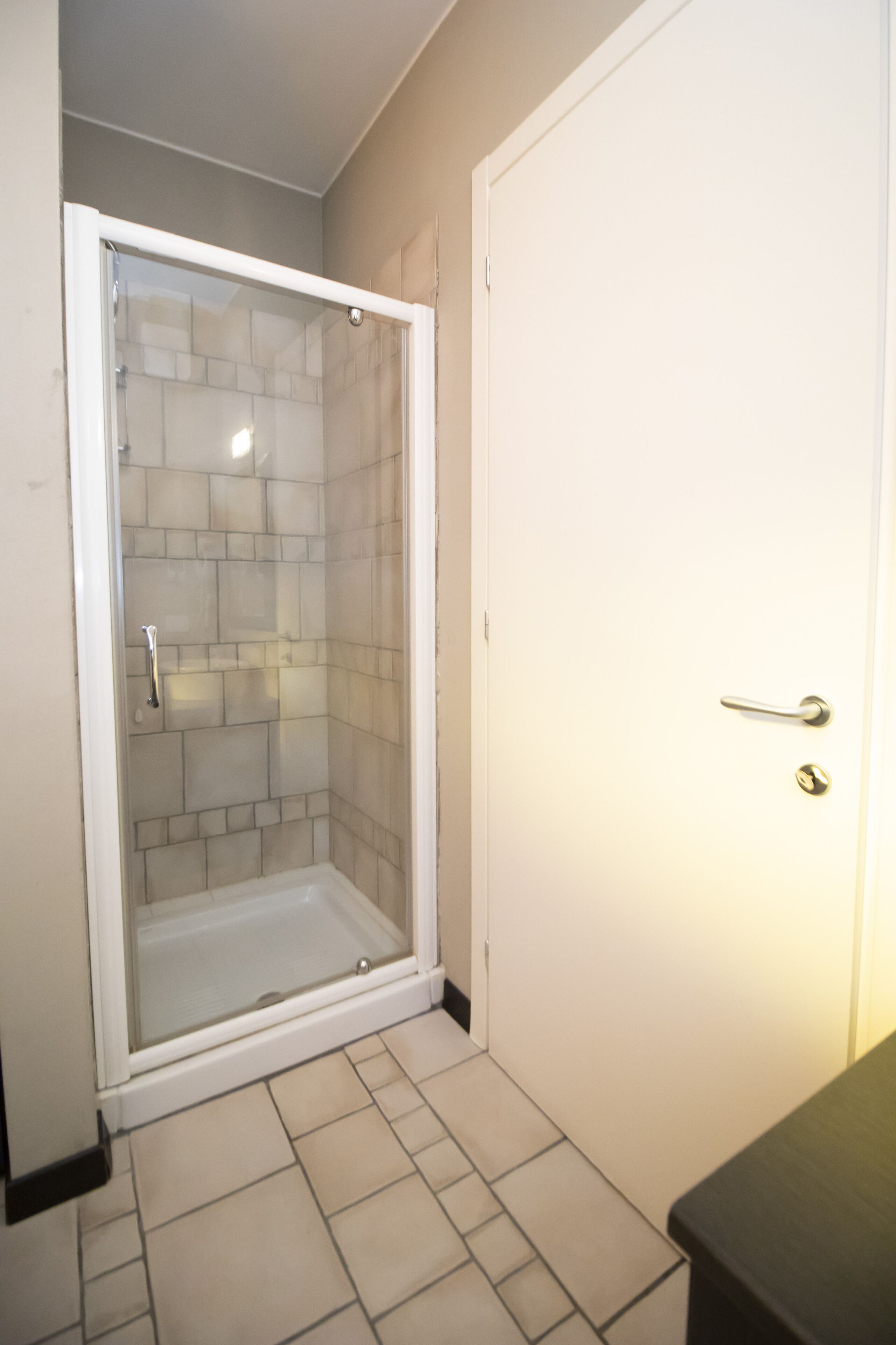 A bathroom with a shower, tiled walls, and a white door.