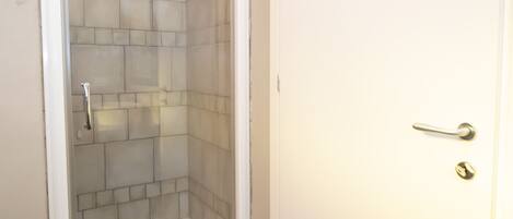 A bathroom with a shower, tiled walls, and a white door.