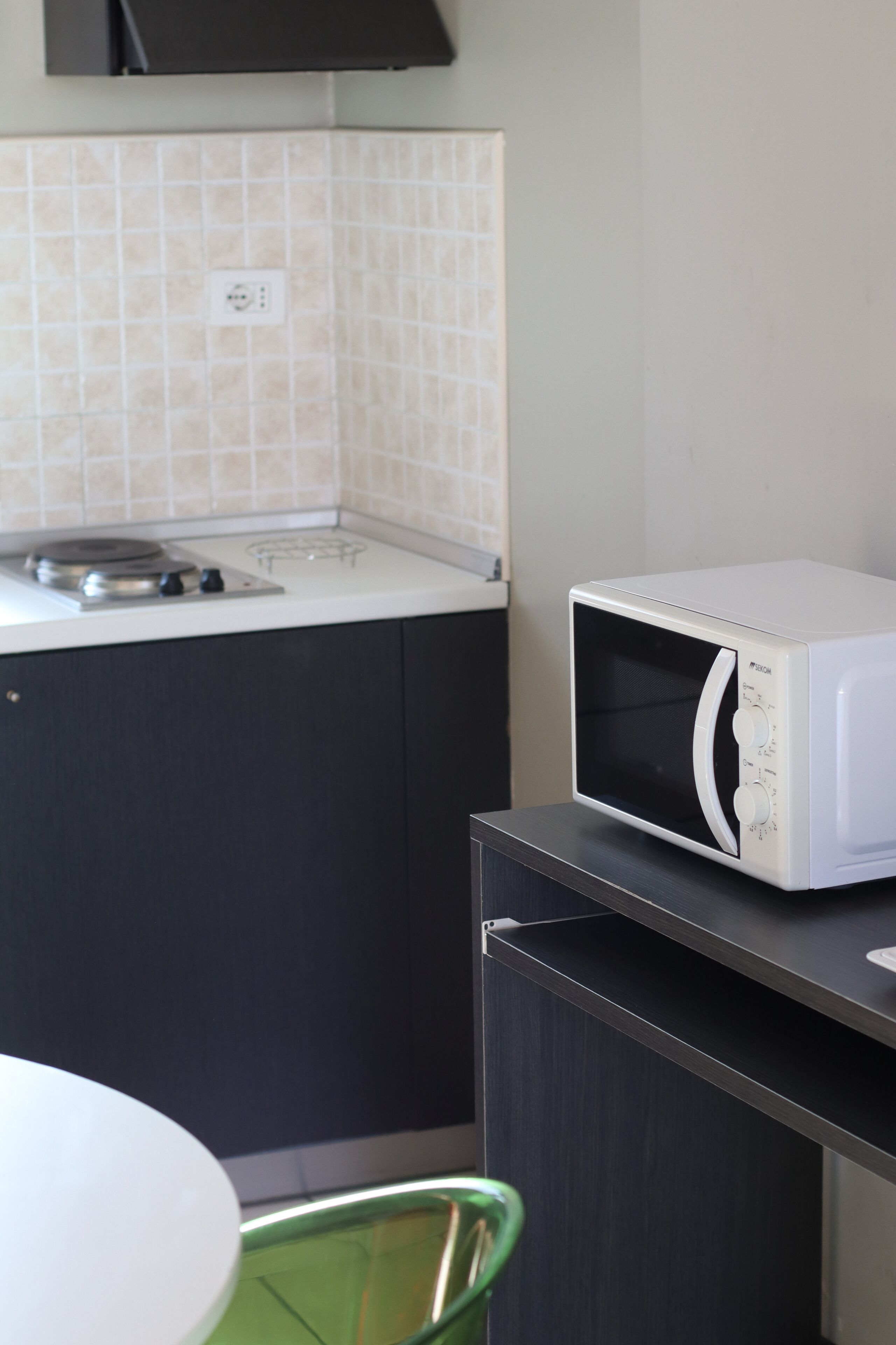 Uma cozinha compacta com micro-ondas em uma bancada, fogão e uma cadeira verde.