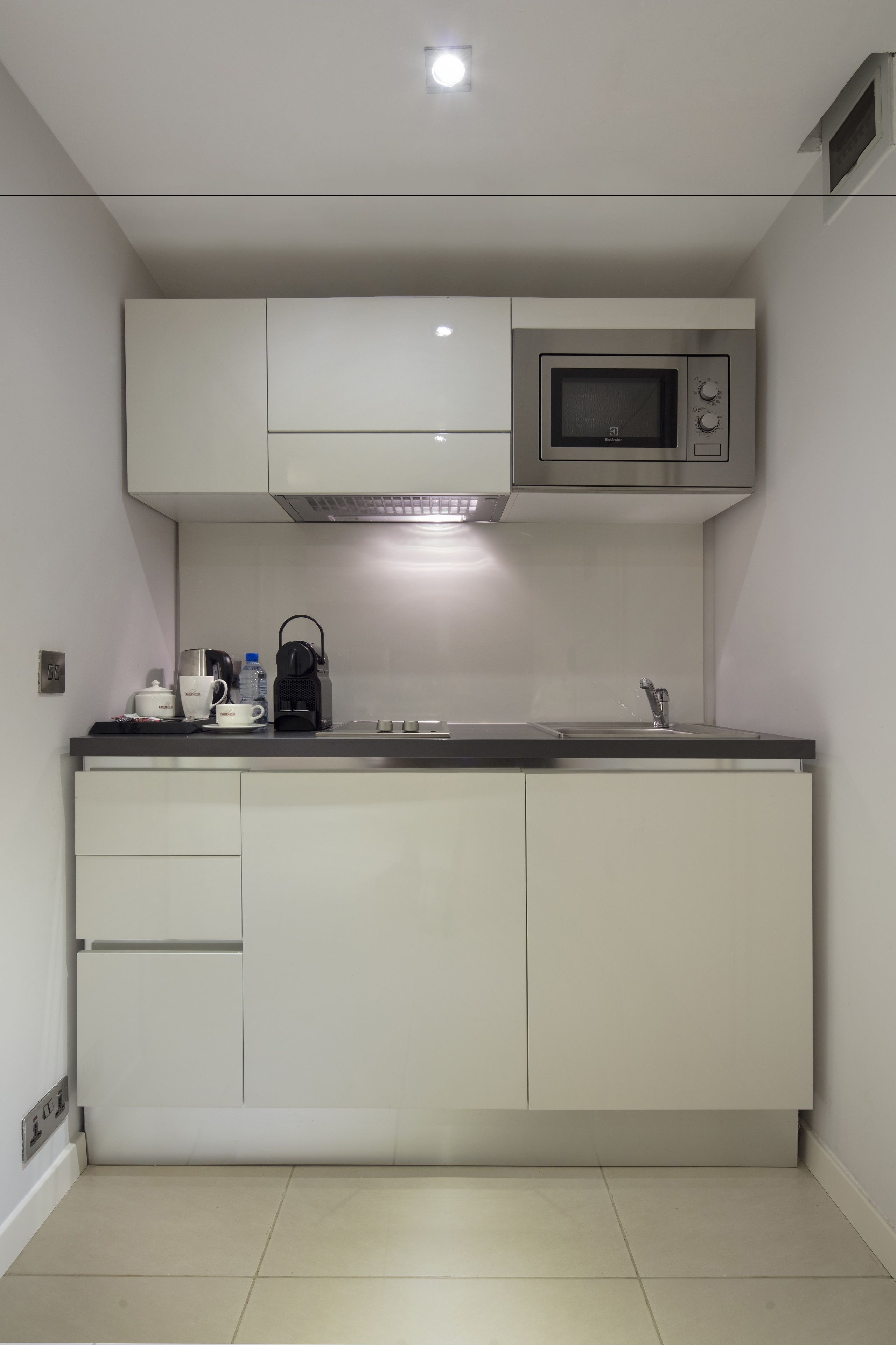 Una cocina moderna con alacenas blancas, un microondas de acero inoxidable y una tetera negra sobre la encimera.