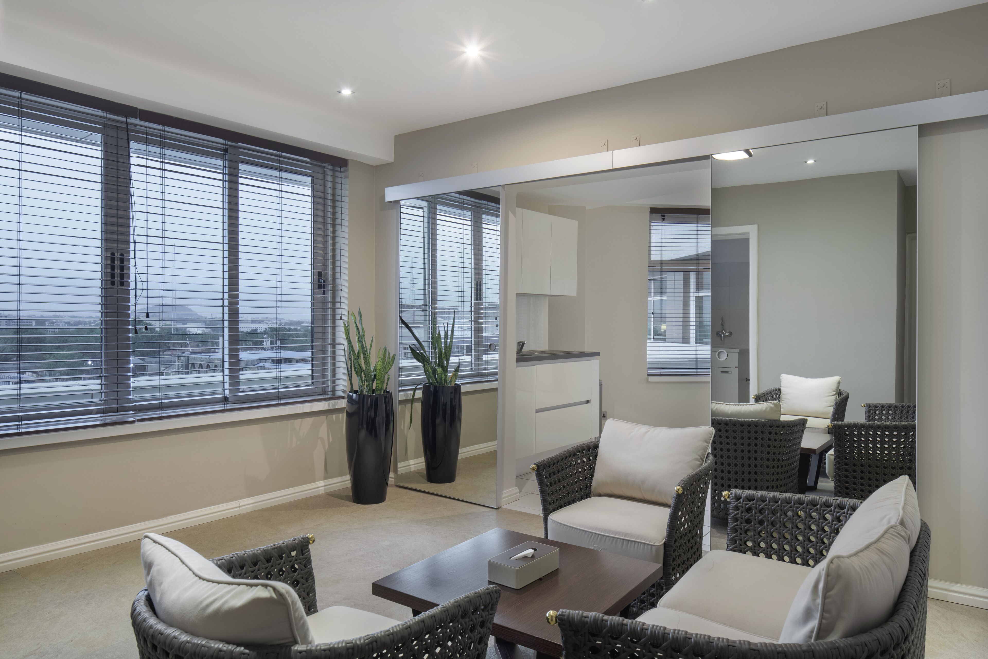 A modern living room with wicker furniture, large windows, and potted plants.