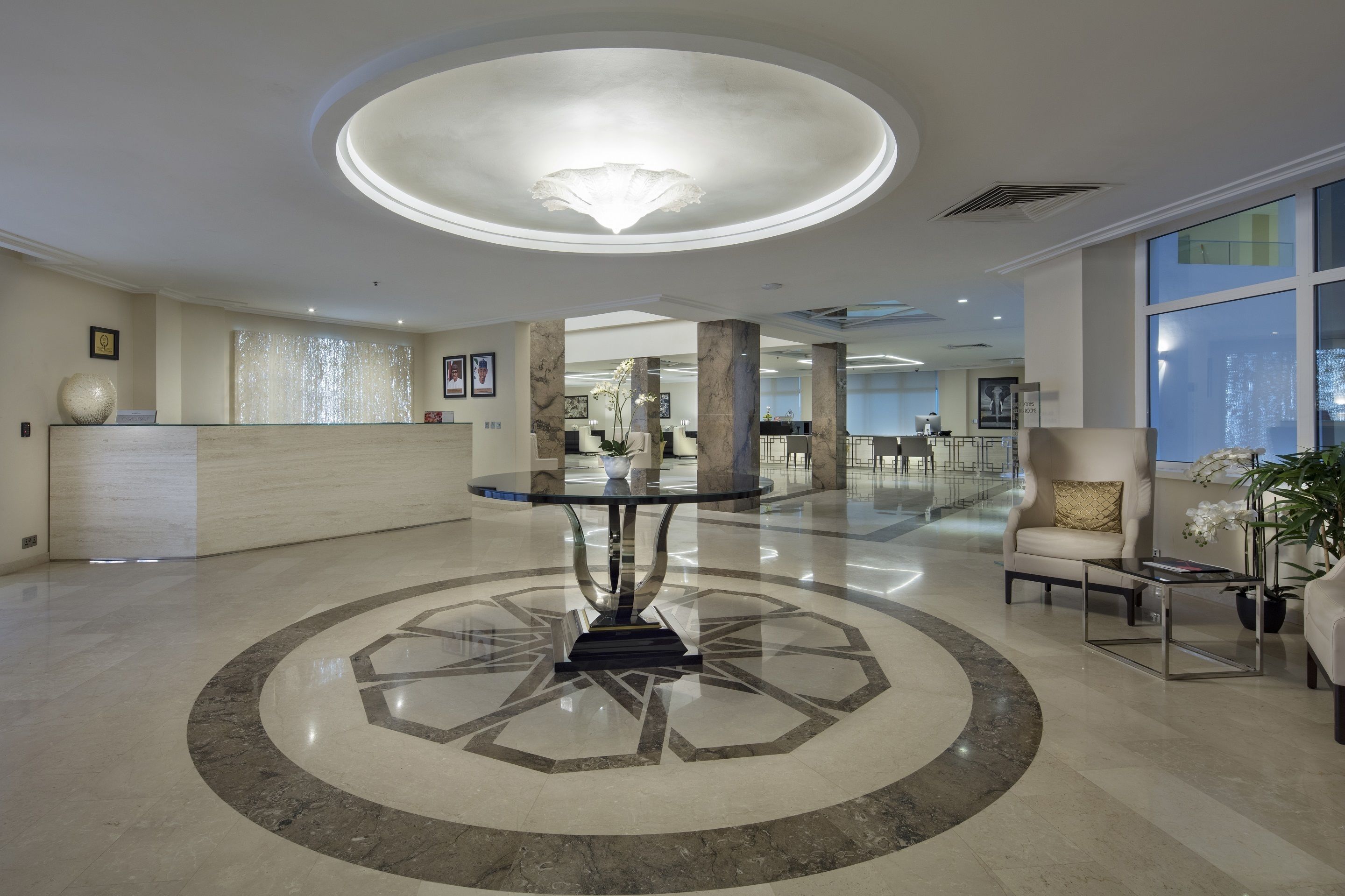 Un hall amplio con una mesa de vidrio en el centro, suelo de mármol y un candelabro moderno.