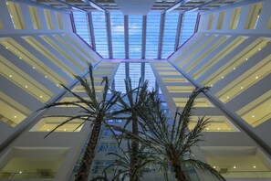 Un atrio espacioso con techos altos, techo de vidrio, palmeras y un diseño arquitectónico moderno.
