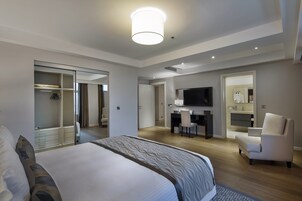 A modern hotel room with a large bed, a desk, a TV, and a walk-in closet.