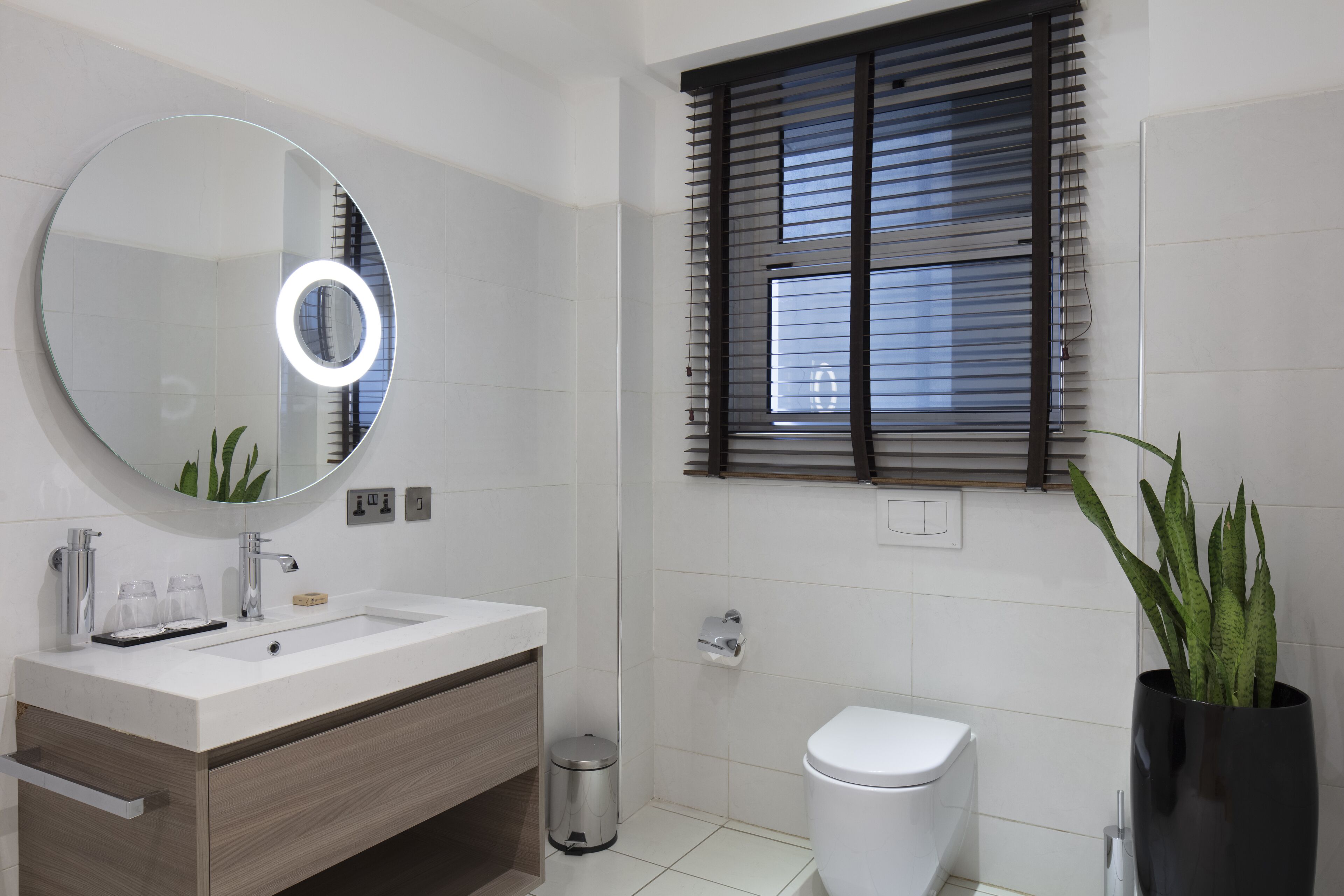 Ein modernes Badezimmer mit rundem Spiegel, weißem Waschbecken und Toilette.