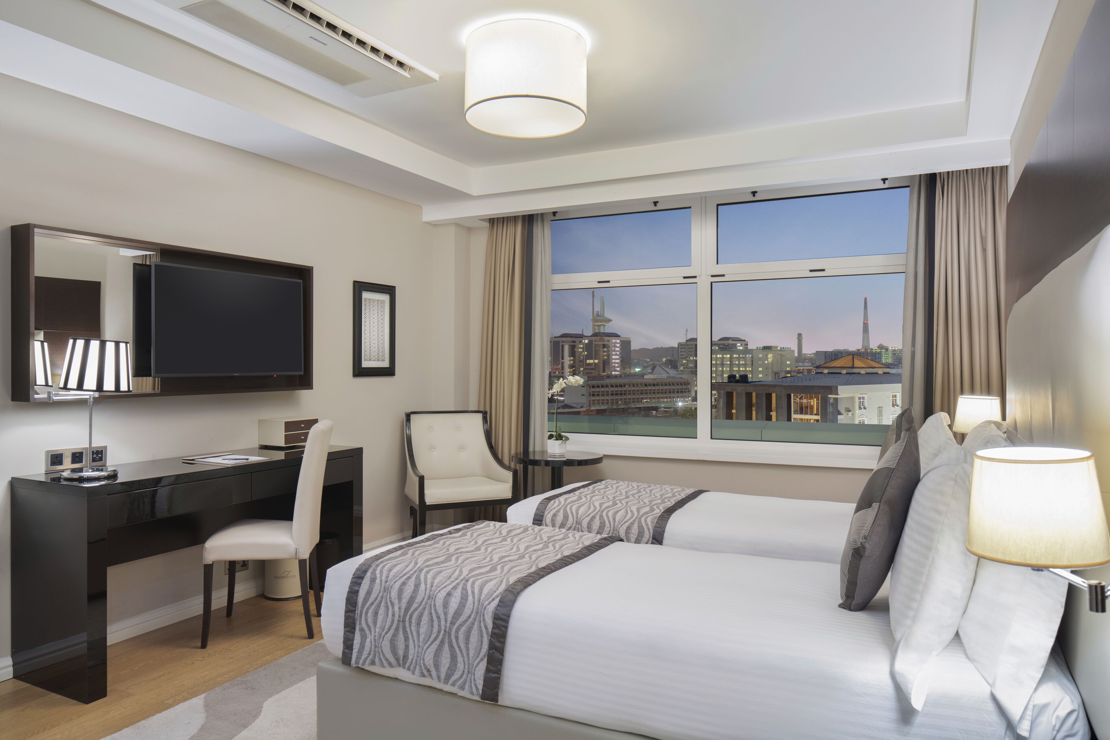 Une chambre d’hôtel avec un grand lit, un bureau, une chaise, une télévision et une fenêtre donnant sur la ville.