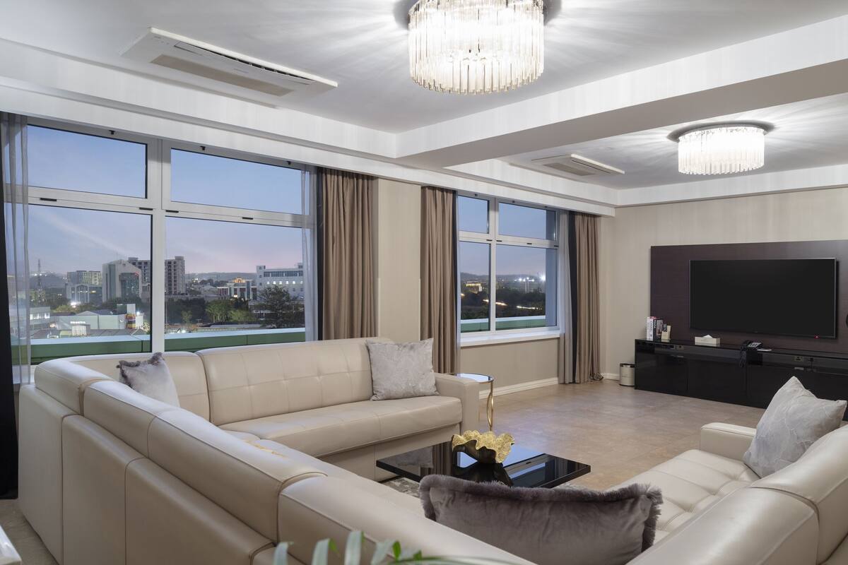 Un salon moderne comprenant un ensemble de canapés, un téléviseur et une grande fenêtre donnant sur la ville.