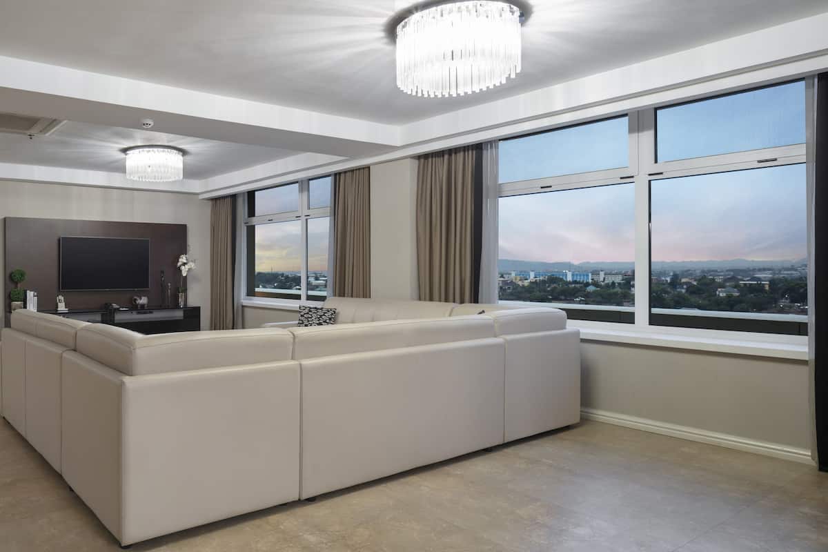 Un salon moderne avec une grande fenêtre, un canapé, un téléviseur et un lustre.