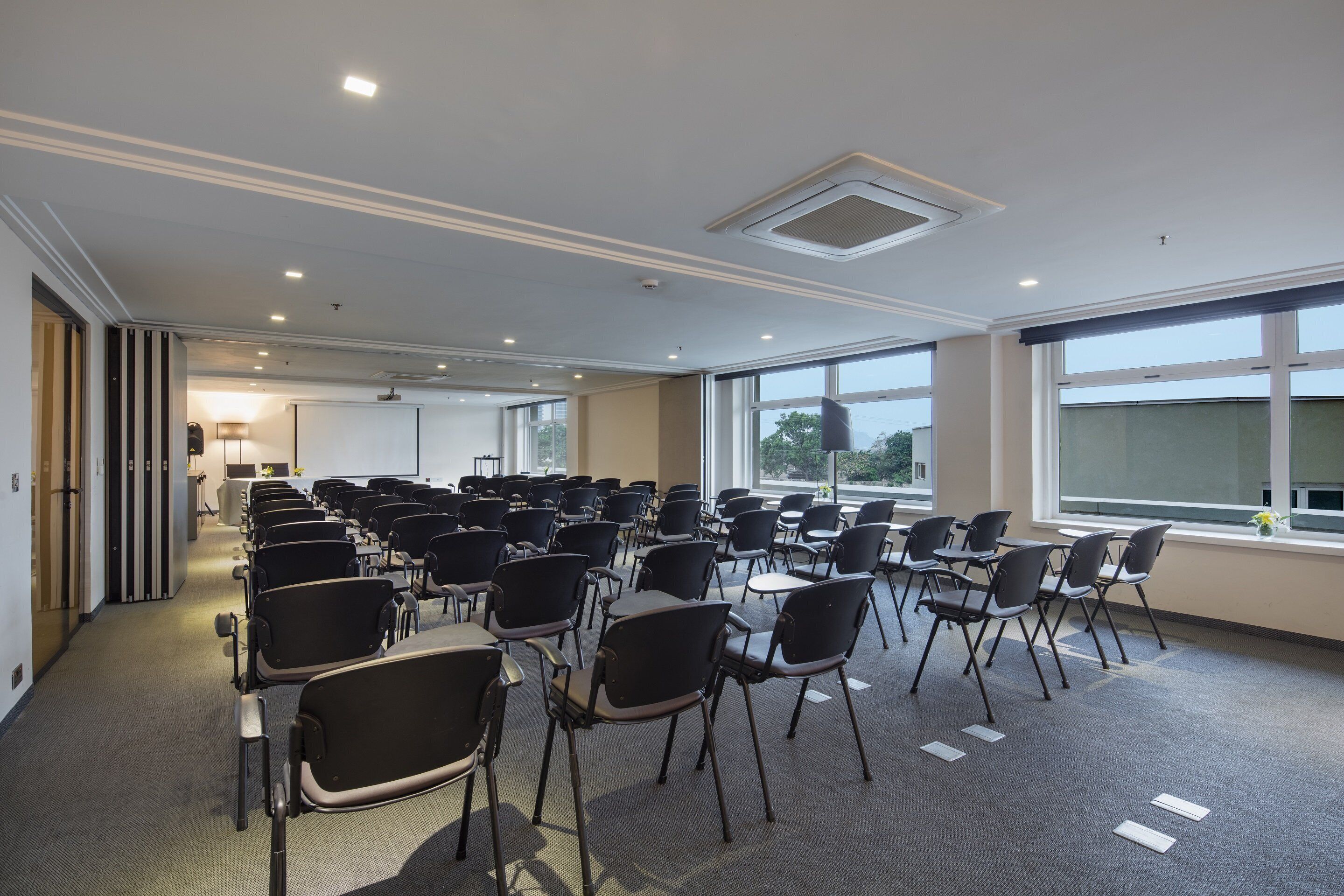 A conference room with rows of chairs, large windows, and a ceiling with recessed lighting.