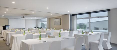 A conference room with multiple tables, white chairs, and a projector screen.