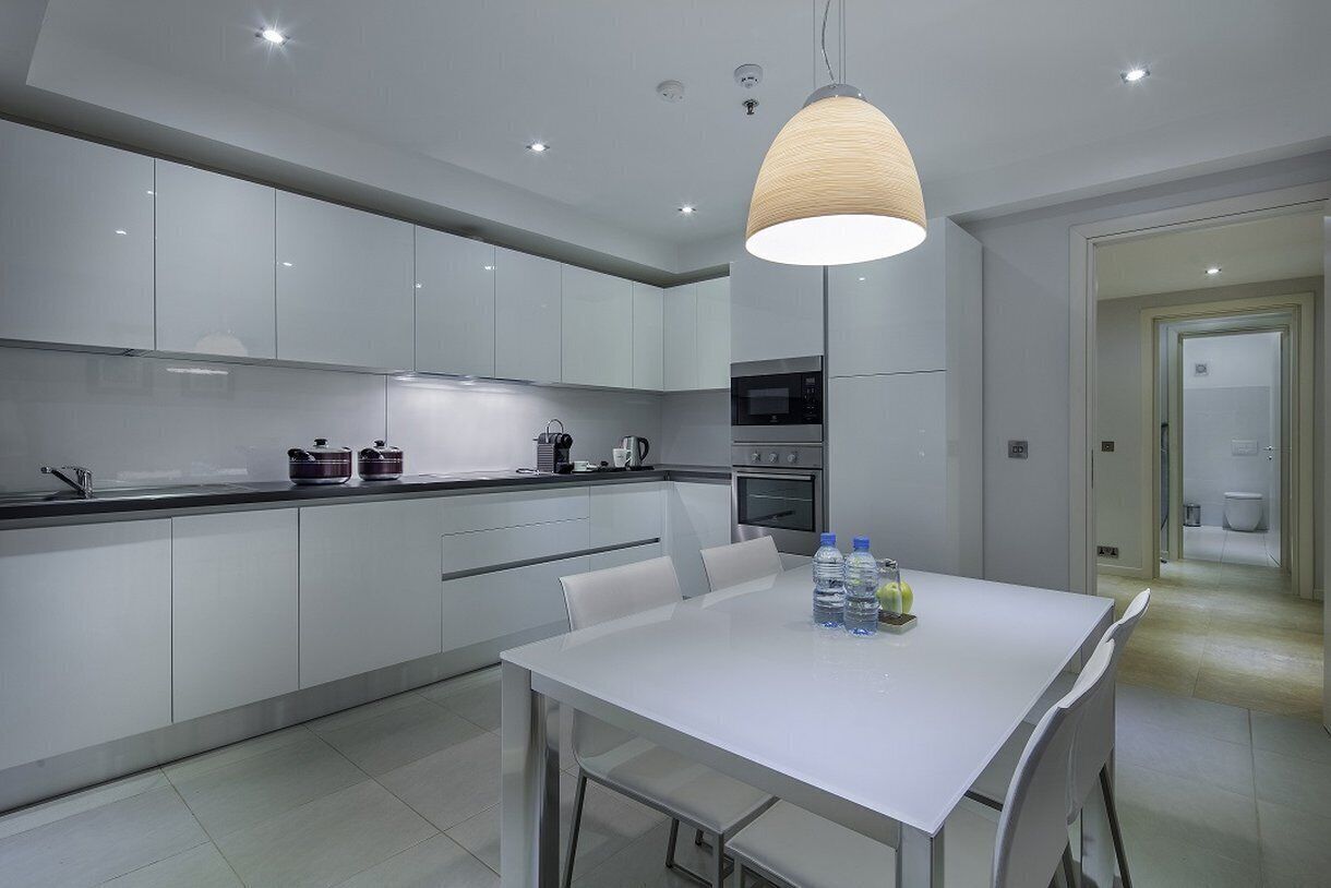 A modern kitchen with white cabinets, a dining table with chairs, and a hanging light fixture.